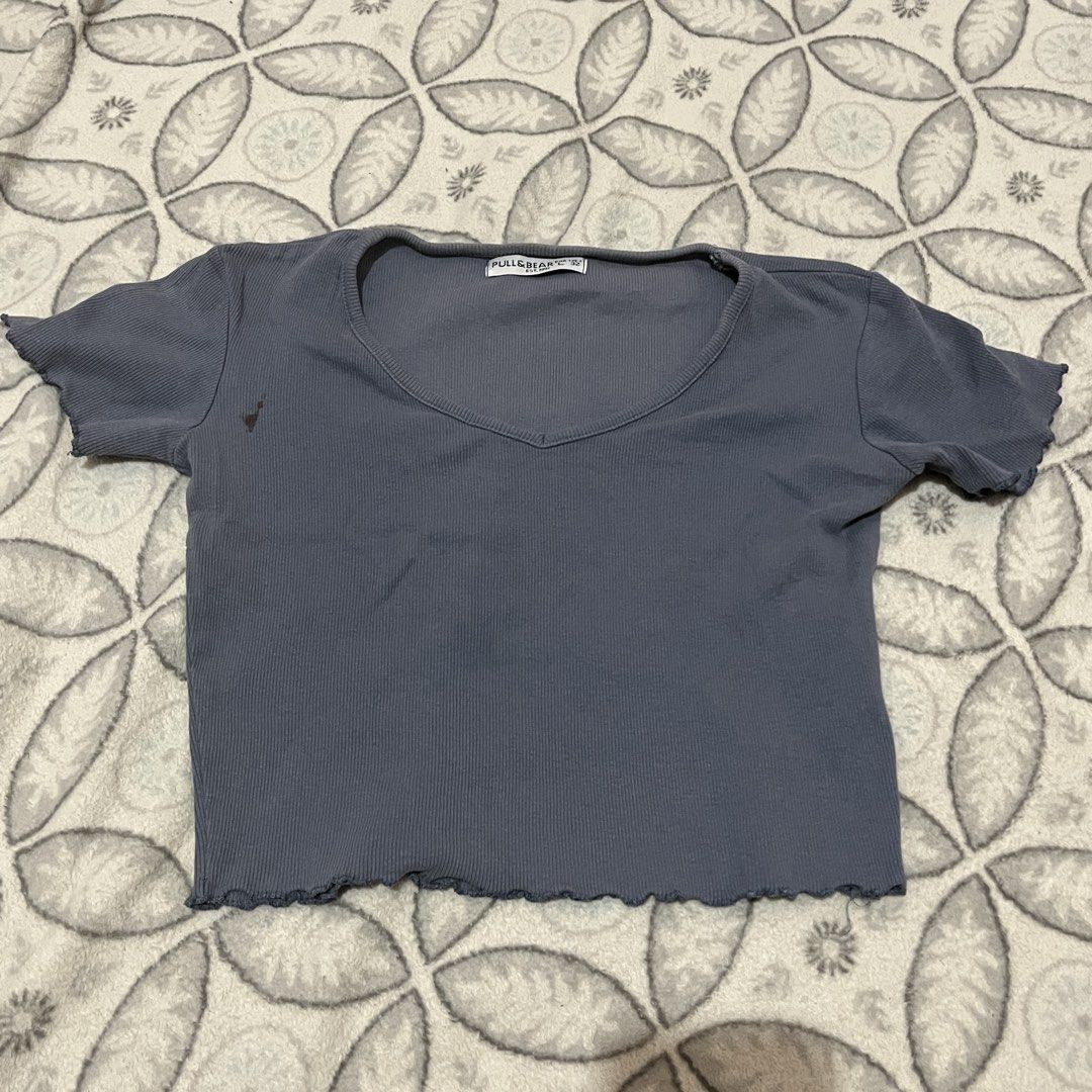 Pull&Bear V-neck Crop Top (Category: Sleeveless) located in Rodriguez. Submitted by decluttrey (Listing ID 1428759998, Image 1). Description: Features a V-neck design and short sleeves. Has a ribbed texture and a wavy hemline. The top is a muted blue-grey color. There is a small stain on the front of the top, but it should come off after washing. Size Large (L) but can fit XS to M Still nego.