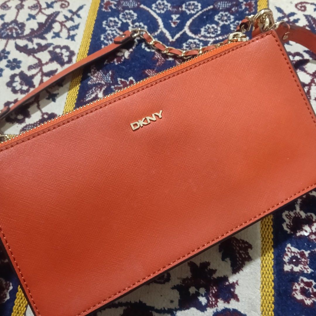 DKNY Orange Crossbody Bag with Chain Strap (Category: Cross-body Bags) located in Mandaluyong City. Submitted by hailey143 (Listing ID 1428883623, Image 2). Description: From US DKNY crossbody bag features a vibrant orange color with a gold chain strap. It includes a matching orange strap for versatile wear. The bag has a zippered closure and includes a DKNY dust bag. The design is sleek and suitable for various occasions. The bag has the DKNY lo