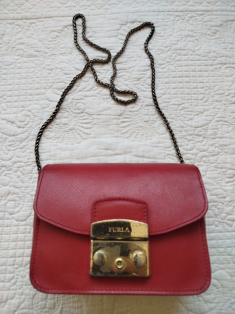 Furla Metropolis Mini Crossbody Bag (Category: Luxury Bags & Wallets) located in Calamba. Submitted by merrymerida (Listing ID 1428839660, Image 1). Description: Red Furla Metropolis Mini crossbody bag with a chain strap. Features a gold-tone clasp closure with the Furla logo. Interior is red with a small pocket. The bag's length is approximately 8 inches. There are some signs of wear on the exterior..