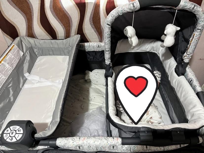 Graco Pack 'n Play Playard with Bassinet (Category: Cots & Cribs) located in San Fernando. Submitted by c.amerrie (Listing ID 1428928433, Image 2). Description: Graco Pack 'n Play playard includes a bassinet and a changing station. It features a mobile with hanging toys and storage pockets. The playard has a gray and white design with patterned fabric..