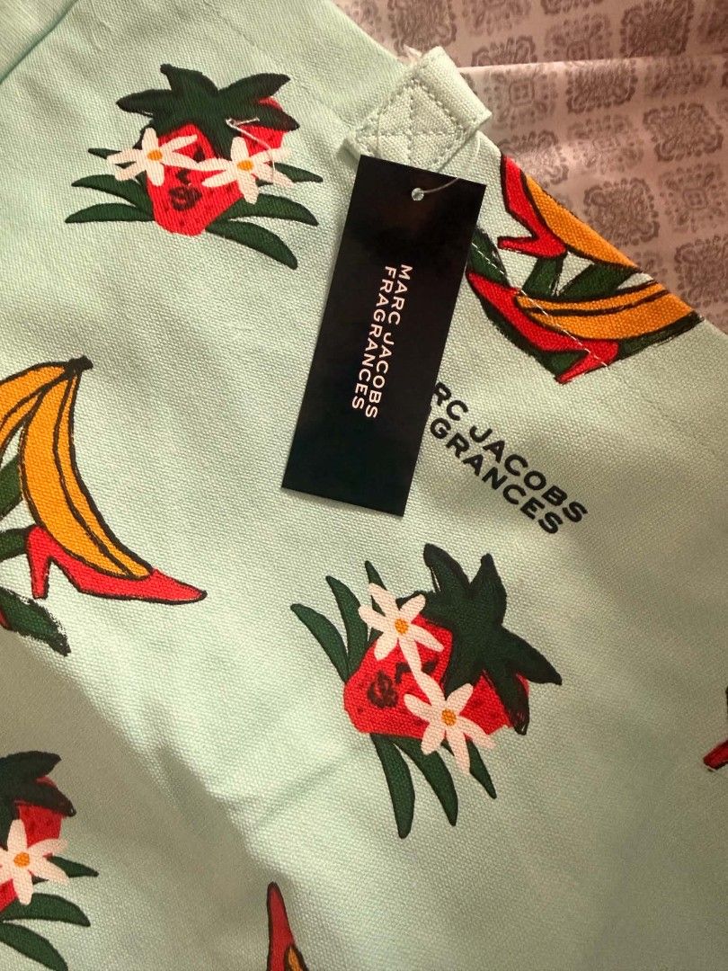 Marc Jacobs Fragrances Tote Bag (Category: Luxury Bags & Wallets) located in Mandaluyong City. Submitted by summerinjun (Listing ID 1428801411, Image 1). Description: Marc Jacobs tote bag features a unique print with strawberries, bananas, and high heels. It has a light blue background and a handle. The tag indicates it's from Marc Jacobs Fragrances. Perfect for carrying your essentials in style..