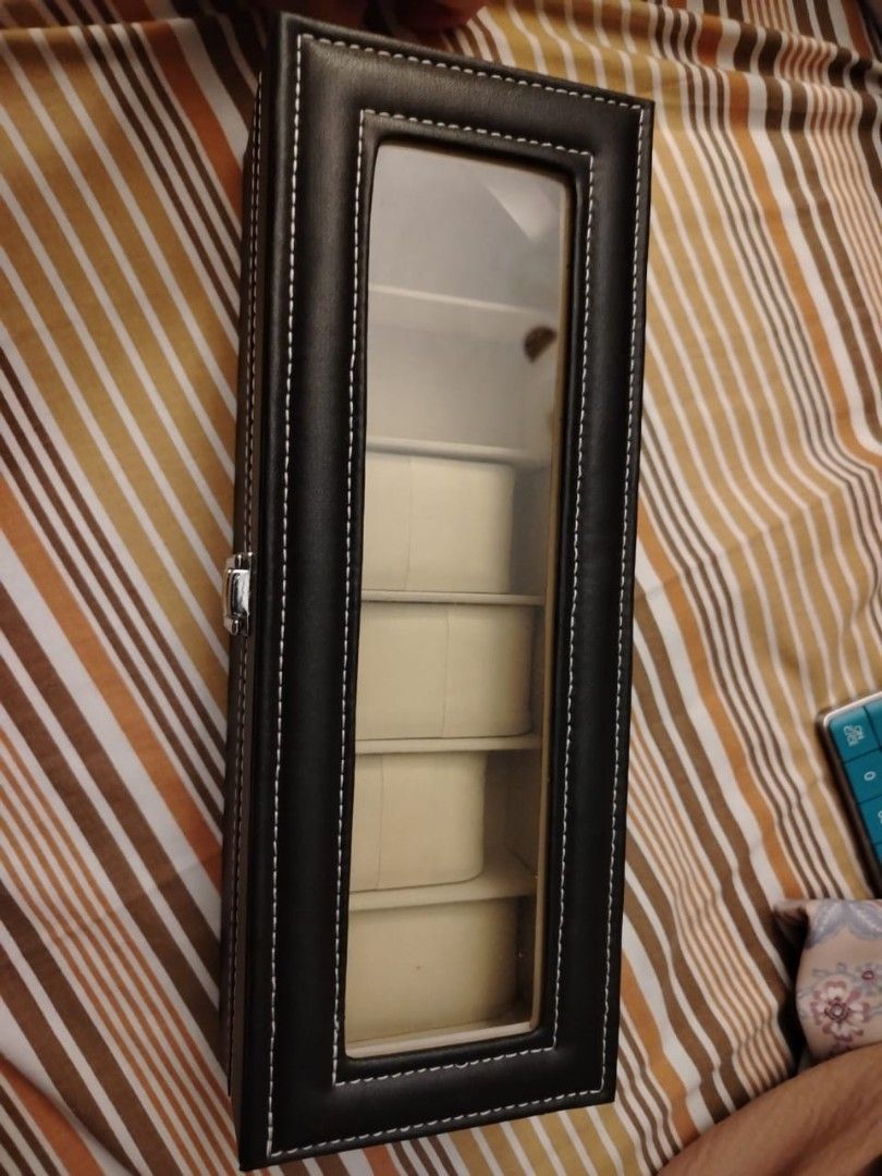 Watch Display Case with Glass Top (Category: Men's Watches) located in Silang. Submitted by juls7a (Listing ID 1428917917, Image 3). Description: Watch display case features a black exterior with white stitching and a clear glass top. It has six individual compartments with beige cushions to hold watches. The case has a silver-colored clasp to secure the lid. The interior is lined with a beige material. May bawas pa basta sure buyer.