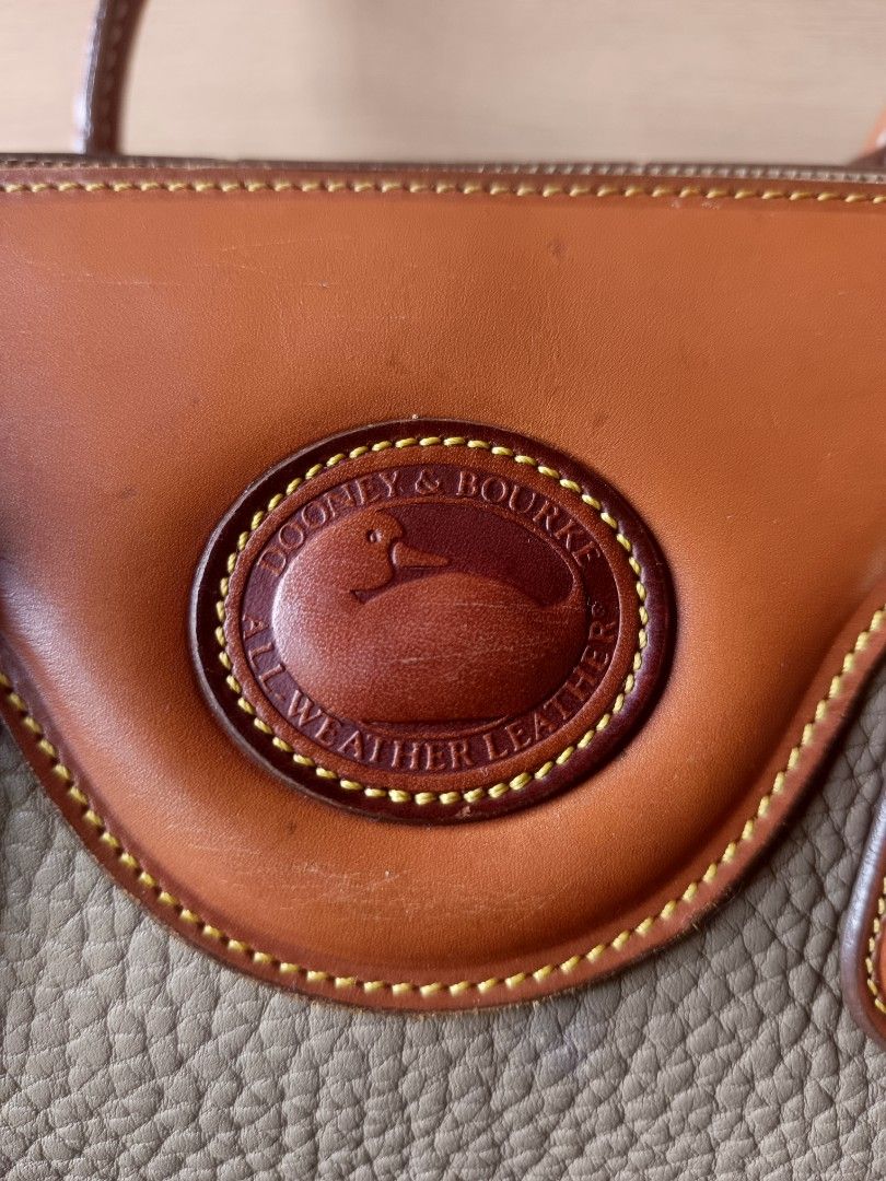 Dooney & Bourke All Weather Doctors Bag (Category: Luxury Bags & Wallets) located in Quezon City. Submitted by thriftymnl_ (Listing ID 1429122056, Image 2). Description: Brand: Dooney & Bourke Style: Satchel / Doctor’s Bag Material: Pebbled All Weather Leather, Smooth Leather Trim, Solid Brass Hardware Color: Taupe (Body) & British Tan (Trim) Features: Iconic leather duck seal on the front, hanging brass duck fob, structured top handles, and full