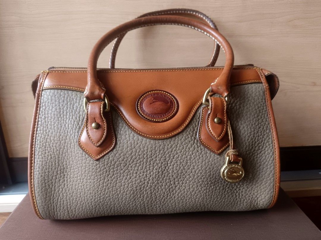 Dooney & Bourke All Weather Doctors Bag (Category: Luxury Bags & Wallets) located in Quezon City. Submitted by thriftymnl_ (Listing ID 1429122056, Image 1). Description: Brand: Dooney & Bourke Style: Satchel / Doctor’s Bag Material: Pebbled All Weather Leather, Smooth Leather Trim, Solid Brass Hardware Color: Taupe (Body) & British Tan (Trim) Features: Iconic leather duck seal on the front, hanging brass duck fob, structured top handles, and full