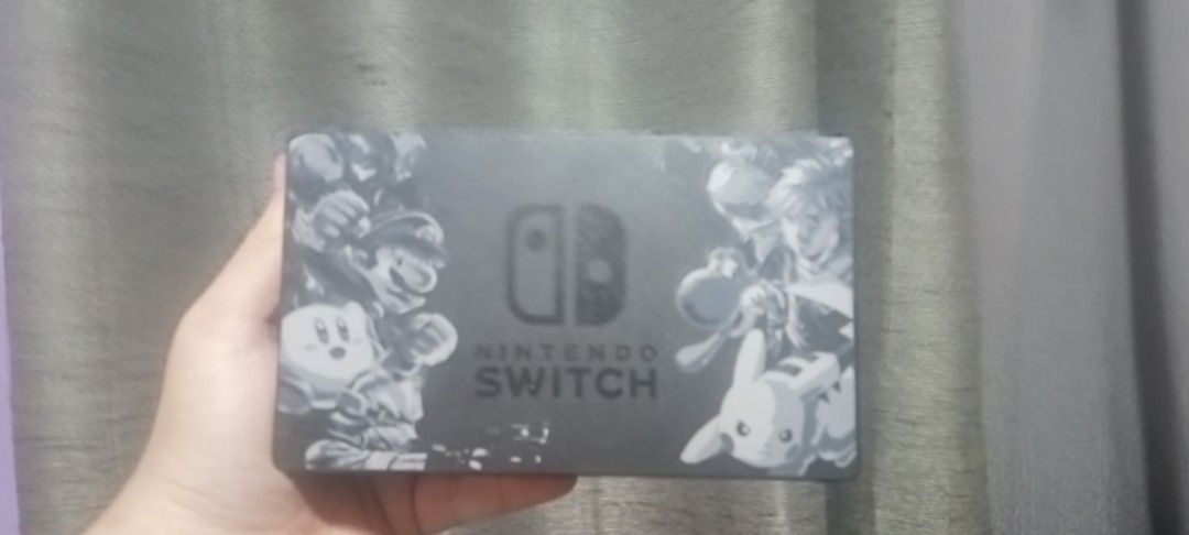 Nintendo Switch Dock Smash Bros Edition (Category: Nintendo) located in Mauban. Submitted by astray00001 (Listing ID 1429021954, Image 2). Description: Nintendo Switch console with a custom design. The console features a black design with various characters on the front. The Nintendo Switch logo is visible..