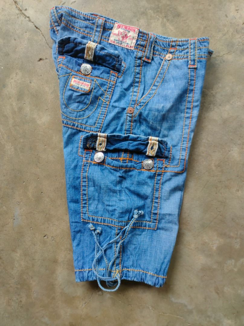 True Religion Denim Cargo Shorts (RARE) (Category: Shorts) located in Baguio. Submitted by pormado (Listing ID 1429107196, Image 3). Description: Authentic True Religion denim cargo shorts. Features multiple pockets and a drawstring at the hem. The shorts have orange stitching and silver hardware. The size tag indicates a size 30. Made of cotton. Perfect for casual wear. Excellent Condition Waist: 32-34 Thigh: 12 Leg Opening: 9.5 (ADJUSTABLE) Len