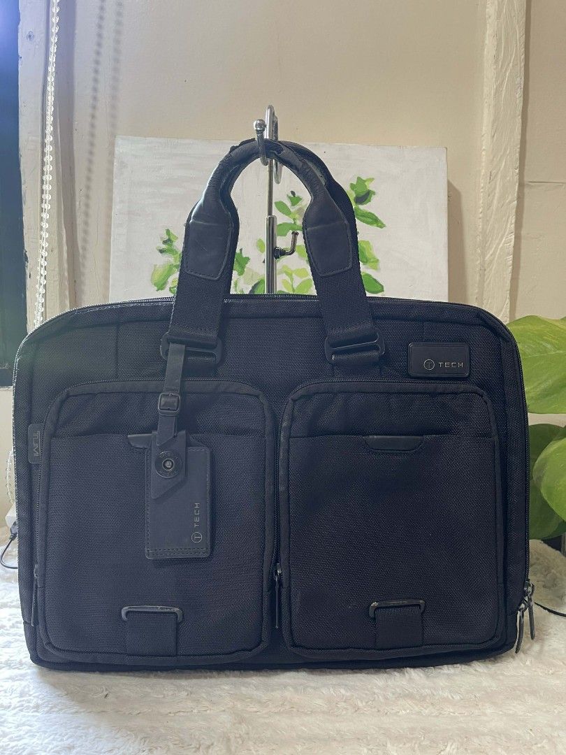 Tumi Black Briefcase laptop bag (Category: Briefcases) located in Naawan. Submitted by twillycalledprelovedbags (Listing ID 1429014732, Image 1). Description: issue: handle, sign of use Black Tumi briefcase with two front pockets. Features a top handle and a detachable tag. The interior is lined with gray fabric. The bag measures approximately 15 inches in width and 12 inches in height..