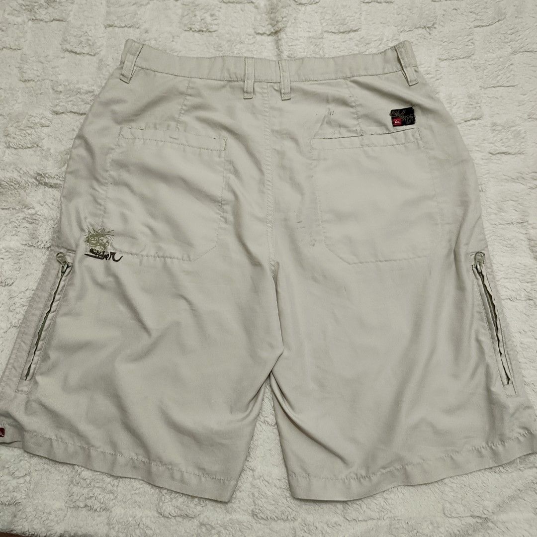 Vintage Quiksilver Beige Shorts (Category: Shorts) located in Santa Cruz. Submitted by fiercegem_1ef7ea (Listing ID 1429157809, Image 2). Description: Beige Quiksilver shorts with multiple pockets, including two side zip pockets. Features the Quiksilver logo embroidered on the side. The shorts have a button and zipper closure. The back of the shorts has two pockets and a small Quiksilver logo..