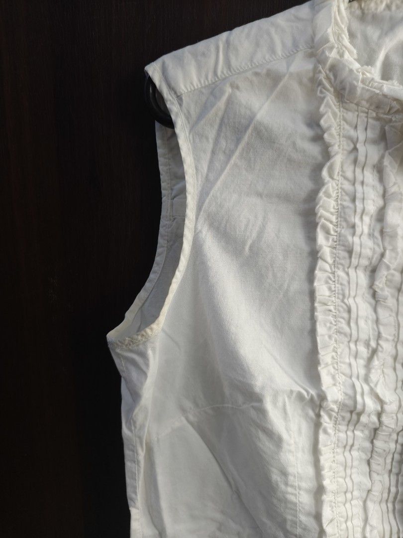 White Sleeveless Blouse with Ruffle Detail (Category: Blouses) located in Taguig. Submitted by declutterwithhannie (Listing ID 1429161522, Image 2). Description: White sleeveless blouse with ruffle detailing down the front. Features a mandarin collar. It has a button-down closure. The blouse is a solid white color. The overall design is simple yet elegant..