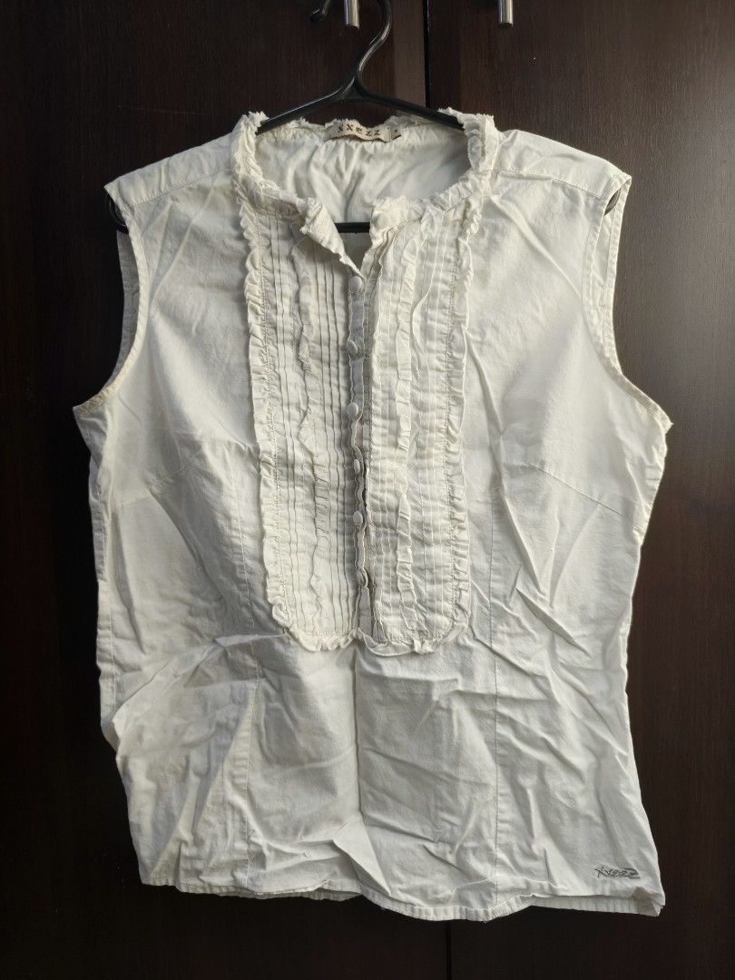 White Sleeveless Blouse with Ruffle Detail (Category: Blouses) located in Taguig. Submitted by declutterwithhannie (Listing ID 1429161522, Image 1). Description: White sleeveless blouse with ruffle detailing down the front. Features a mandarin collar. It has a button-down closure. The blouse is a solid white color. The overall design is simple yet elegant..