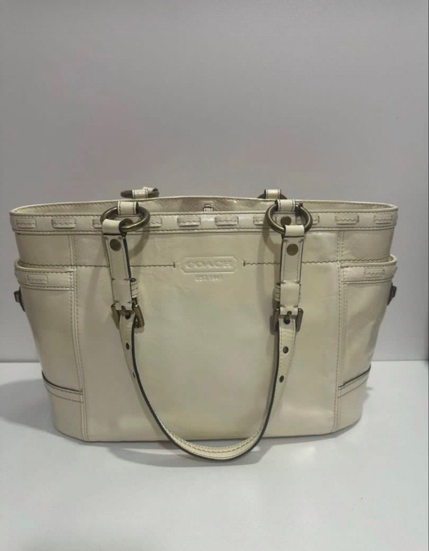 Coach Cream Leather Tote Bag (Category: Luxury Bags & Wallets) located in Mandaluyong City. Submitted by mnlmeetup (Listing ID 1424472812, Image 2). Description: Cream-colored Coach tote bag. Features a main compartment with a patterned lining and a small attached tag. Includes two exterior side pockets. The bag has double handles and metal hardware. The Coach logo is visible on the front. The bag has a rectangular shape with a flat bottom..