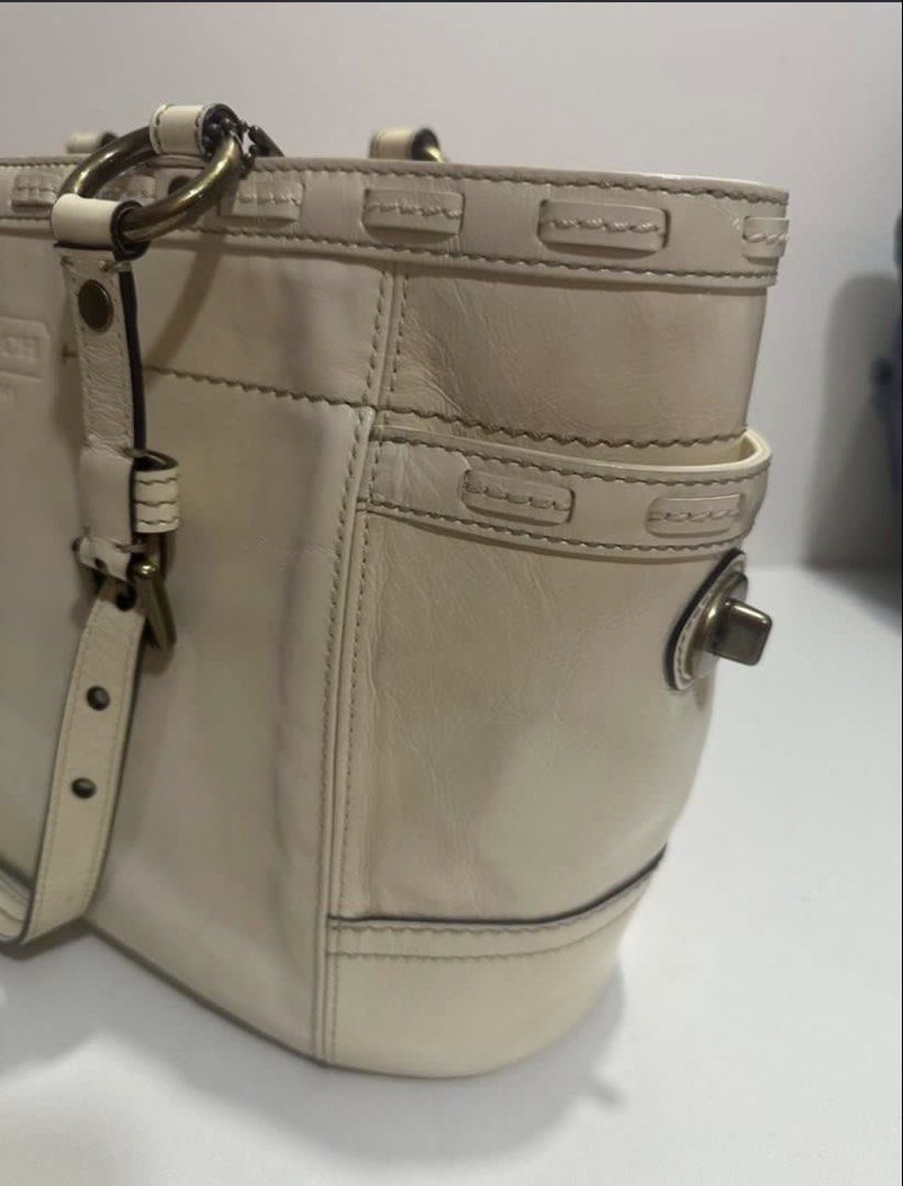 Coach Cream Leather Tote Bag (Category: Luxury Bags & Wallets) located in Mandaluyong City. Submitted by mnlmeetup (Listing ID 1424472812, Image 3). Description: Cream-colored Coach tote bag. Features a main compartment with a patterned lining and a small attached tag. Includes two exterior side pockets. The bag has double handles and metal hardware. The Coach logo is visible on the front. The bag has a rectangular shape with a flat bottom..