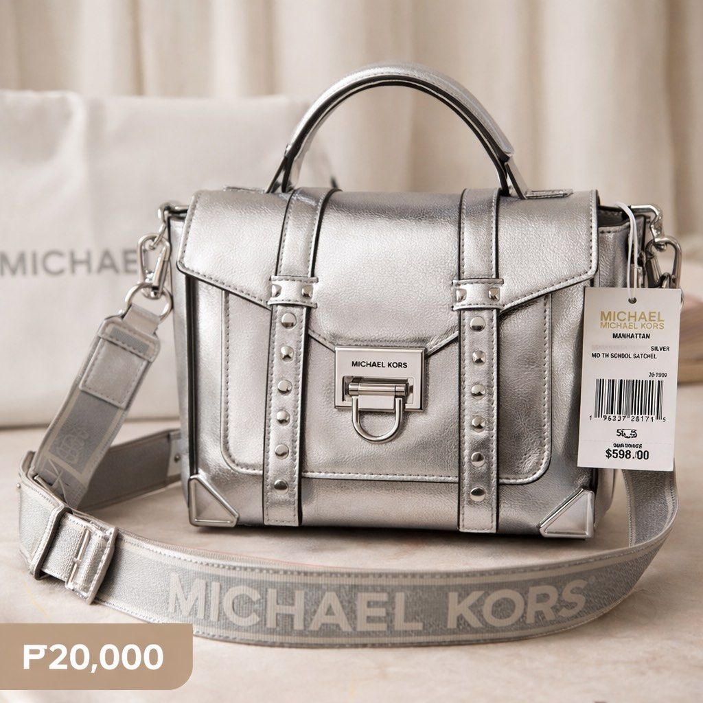 Michael Kors Manhattan MD TH School Satchel (Category: Luxury Bags & Wallets) located in Pagadian. Submitted by maximaxcollection (Listing ID 1424454567, Image 1). Description: Silver Michael Kors Manhattan MD TH School Satchel. Features a top handle and a detachable shoulder strap with the Michael Kors logo. The bag has a flap closure with a metal clasp. The original price tag is still attached, showing a price of $598.00. The bag has a silver f