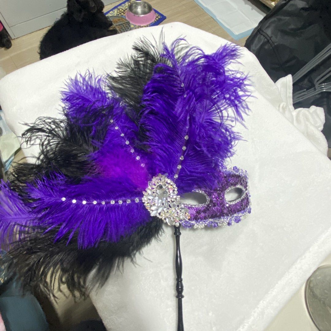 Purple Feathered Masquerade Mask (Category: Other Accessories) located in Marikina City. Submitted by creatingmorespace (Listing ID 1424428622, Image 3). Description: - Masquerade mask with vibrant purple and black feathers. - Decorated with sparkling rhinestones and sequins. - Features a black handle for easy holding. - Perfect for parties, events, and costumes. - Bought at P2,000.
