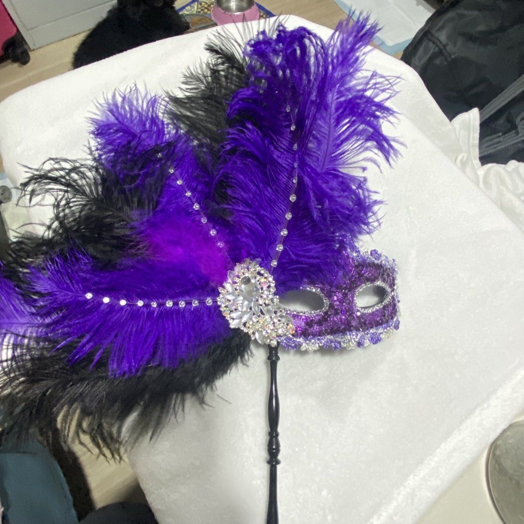 Purple Feathered Masquerade Mask (Category: Other Accessories) located in Marikina City. Submitted by creatingmorespace (Listing ID 1424428622, Image 2). Description: - Masquerade mask with vibrant purple and black feathers. - Decorated with sparkling rhinestones and sequins. - Features a black handle for easy holding. - Perfect for parties, events, and costumes. - Bought at P2,000.