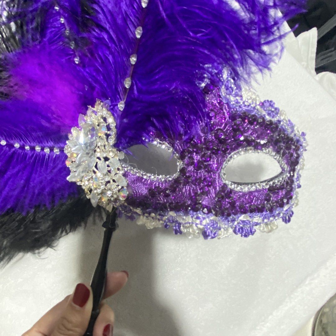 Purple Feathered Masquerade Mask (Category: Other Accessories) located in Marikina City. Submitted by creatingmorespace (Listing ID 1424428622, Image 1). Description: - Masquerade mask with vibrant purple and black feathers. - Decorated with sparkling rhinestones and sequins. - Features a black handle for easy holding. - Perfect for parties, events, and costumes. - Bought at P2,000.