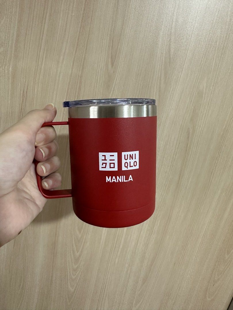 Uniqlo Manila Mug with Lid (Category: Coffee & Tea Tableware) located in Manila. Submitted by aj.honey (Listing ID 1424468080, Image 1). Description: - Uniqlo Manila mug - Red color - Features Uniqlo logo and "MANILA" text - Made of metal - Includes handle and lid - Suitable for hot or cold beverages.