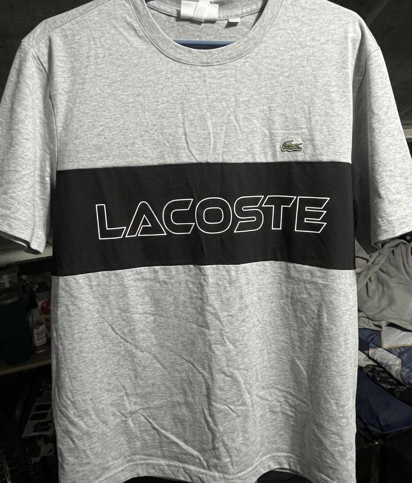 Lacoste Colorblock T-shirt (Category: Tshirts & Polo Shirts ) located in Taguig. Submitted by random.stuff31 (Listing ID 1429236655, Image 1). Description: Gray Lacoste t-shirt with a black colorblock across the chest. Features the Lacoste logo on the chest. The word "LACOSTE" is printed in white on the black colorblock. It has a crew neck and short sleeves. FR 6 US XL.