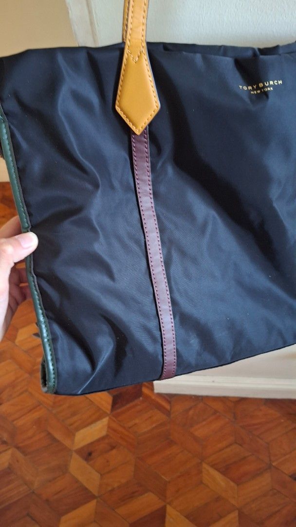 ORIGINAL Tory Burch Nylon Tote Bag (Category: Luxury Bags & Wallets) located in Las Pinas. Submitted by mgr29 (Listing ID 1429172813, Image 3). Description: FLAWS: DOG BITE - USED ELECTRIC TAPE TO HIDE AND USED A SCARF TO WRAP THE HANDLE. SLIGHT PEELING IN ONE OF THE HANDLES USED TWICE AND STORED FOR A LONG TIEM. Black nylon tote bag from Tory Burch. Features leather straps and accents in brown and orange. Includes a patterned scarf tied to the h