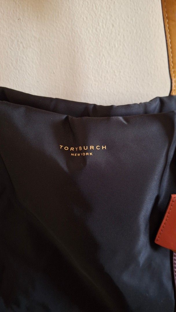 ORIGINAL Tory Burch Nylon Tote Bag (Category: Luxury Bags & Wallets) located in Las Pinas. Submitted by mgr29 (Listing ID 1429172813, Image 2). Description: FLAWS: DOG BITE - USED ELECTRIC TAPE TO HIDE AND USED A SCARF TO WRAP THE HANDLE. SLIGHT PEELING IN ONE OF THE HANDLES USED TWICE AND STORED FOR A LONG TIEM. Black nylon tote bag from Tory Burch. Features leather straps and accents in brown and orange. Includes a patterned scarf tied to the h