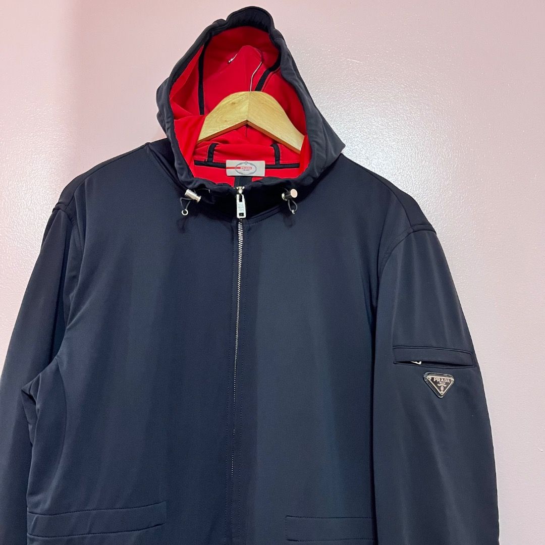 Prada Sport Jacket - Black and Red Lining (Category: Luxury Apparel) located in Bacolod City. Submitted by boujee.wardrobes (Listing ID 1429319991, Image 2). Description: Prada hooded jacket. Features a black exterior with a red interior lining. Includes a zip closure, a Prada logo on the sleeve, and a size tag inside. The jacket has a hood with adjustable drawstrings and a zip pocket. Size is Tg.50. 27L 21.5W.