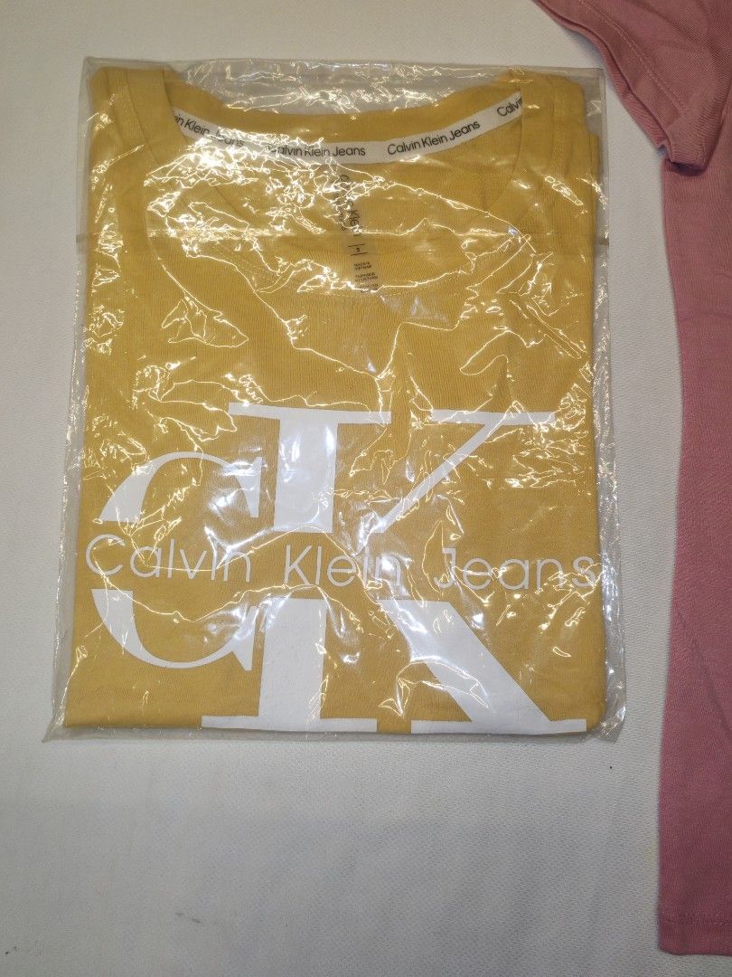 Calvin Klein Jeans T-shirts (Category: Shirts) located in Quezon City. Submitted by rowem (Listing ID 1429476473, Image 3). Description: These Calvin Klein Jeans t-shirts are available in yellow and pink. They feature the Calvin Klein Jeans logo on the front. The t-shirts appear to be unworn and are still in their original packaging. They have a classic crew neck design..