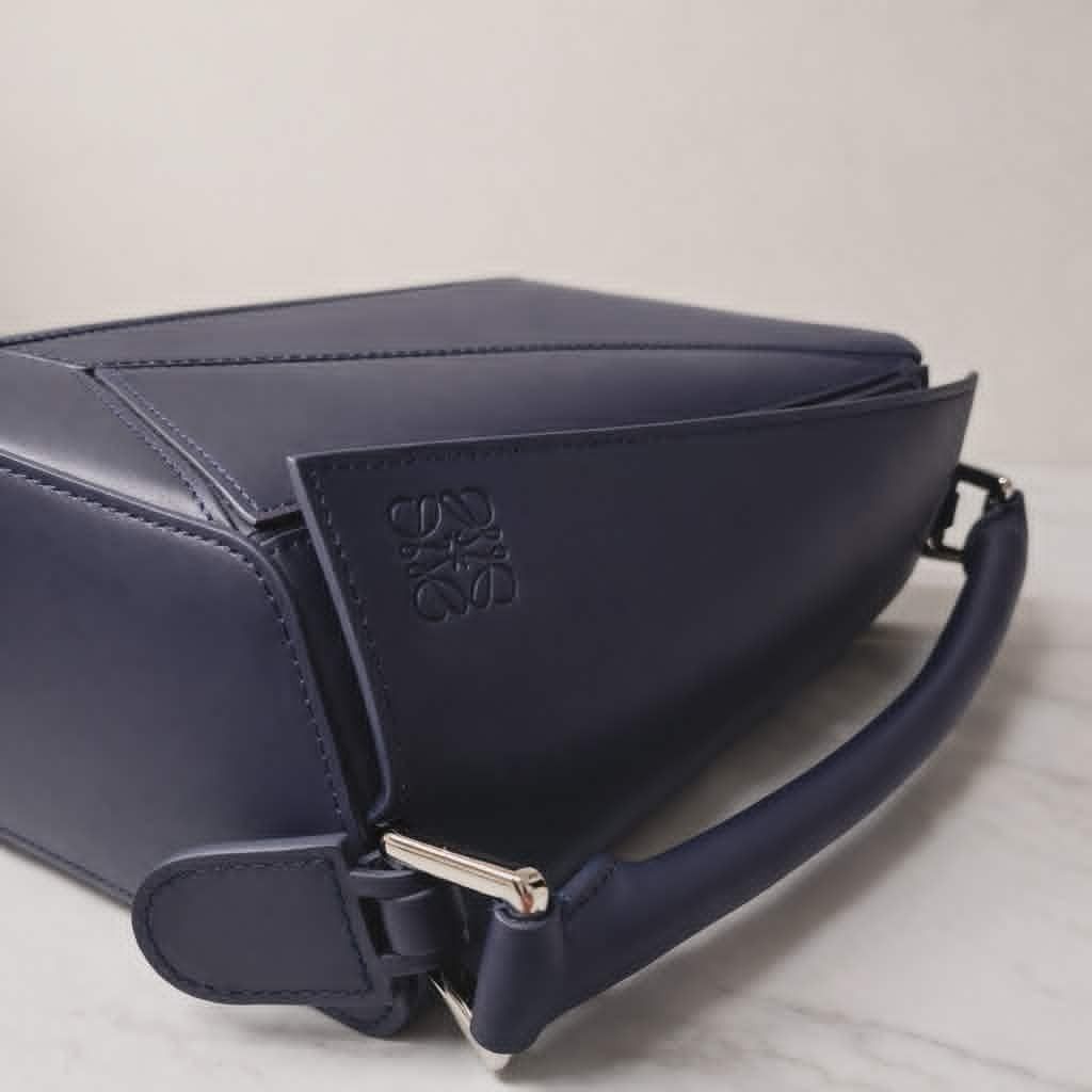 Loewe Puzzle Edge Small Bag Navy Blue (Category: Luxury Bags & Wallets) located in Cebu City. Submitted by theluxxaffair (Listing ID 1429484766, Image 3). Description: Authentic Loewe Puzzle Edge Small bag crafted in navy blue calfskin leather. It features a top handle and a detachable shoulder strap with the Loewe logo. The bag has a zipper closure, and the Loewe logo is embossed on the side. It includes a dust bag and a box. Length: 24 cm Heigh