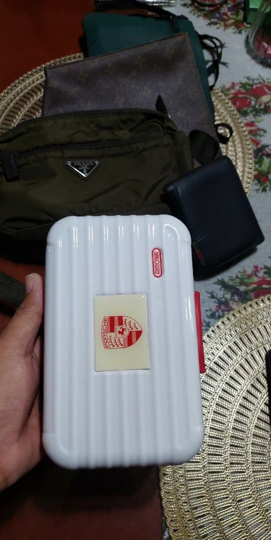 Porsche Rimowa (Category: Luxury Bags & Wallets) located in Puerto Princesa. Submitted by YeSurJOMS (Listing ID 1429364798, Image 1). Description: White Porsche Design pencil case with a red zipper and trim. Features the Porsche logo on the front. The interior is black. The case has a rectangular shape with a ridged design on the front and back. The zipper has the Porsche Design logo..