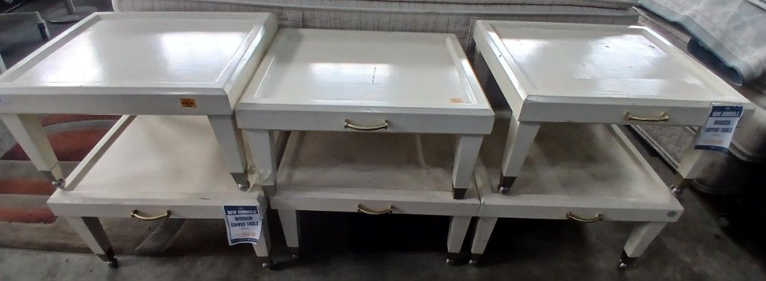 Wooden Coffee Table (Category: Tables & Sets) located in Manila. Submitted by sc_arvin (Listing ID 1429370502, Image 1). Description: Set of white side tables. Each table features a drawer with a gold-colored handle and a lower shelf for storage. The tables have a square top and are supported by four legs. Some legs have wheels. Perfect for living rooms or bedrooms..