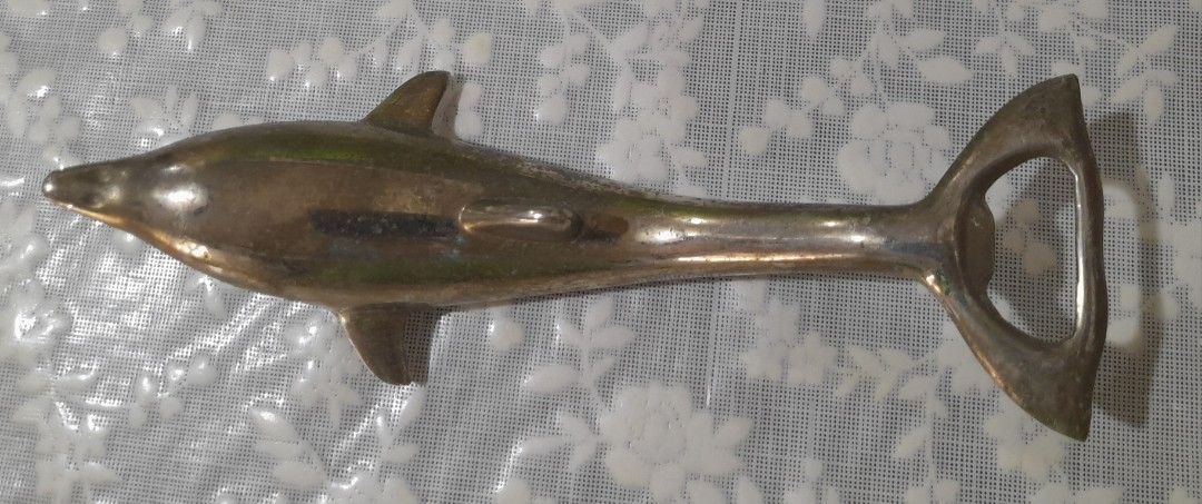 1970's Dolphin Bottle Opener: Nautical Barware (Category: Vintage Collectibles) located in Manila. Submitted by miamiga (Listing ID 1424622325, Image 1). Description: - Vintage dolphin-shaped bottle opener - Silver-colored finish - Includes a bottle opener at the tail - Underside is used for twist off caps - Detailed dolphin design -No longer in mint condition -With signs of age, usage, and stains Size: 6.5".