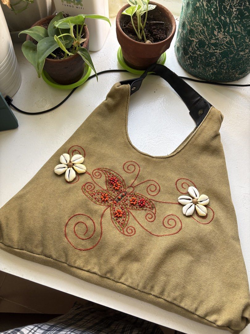 Fairycore Embroidered Canvas Handbag with Shell Accents (Category: Shoulder Bags) located in Pasay City. Submitted by casy23 (Listing ID 1424570589, Image 1). Description: ‼️ Price can be slight nego pa rin‼️ - Canvas handbag with embroidered butterfly design - Adorned with shell accents - Black leather handle (see image for tiny damage) - Two zippered pockets on the back - Unique triangular shape RFS: Outgrowing my old stuff na.