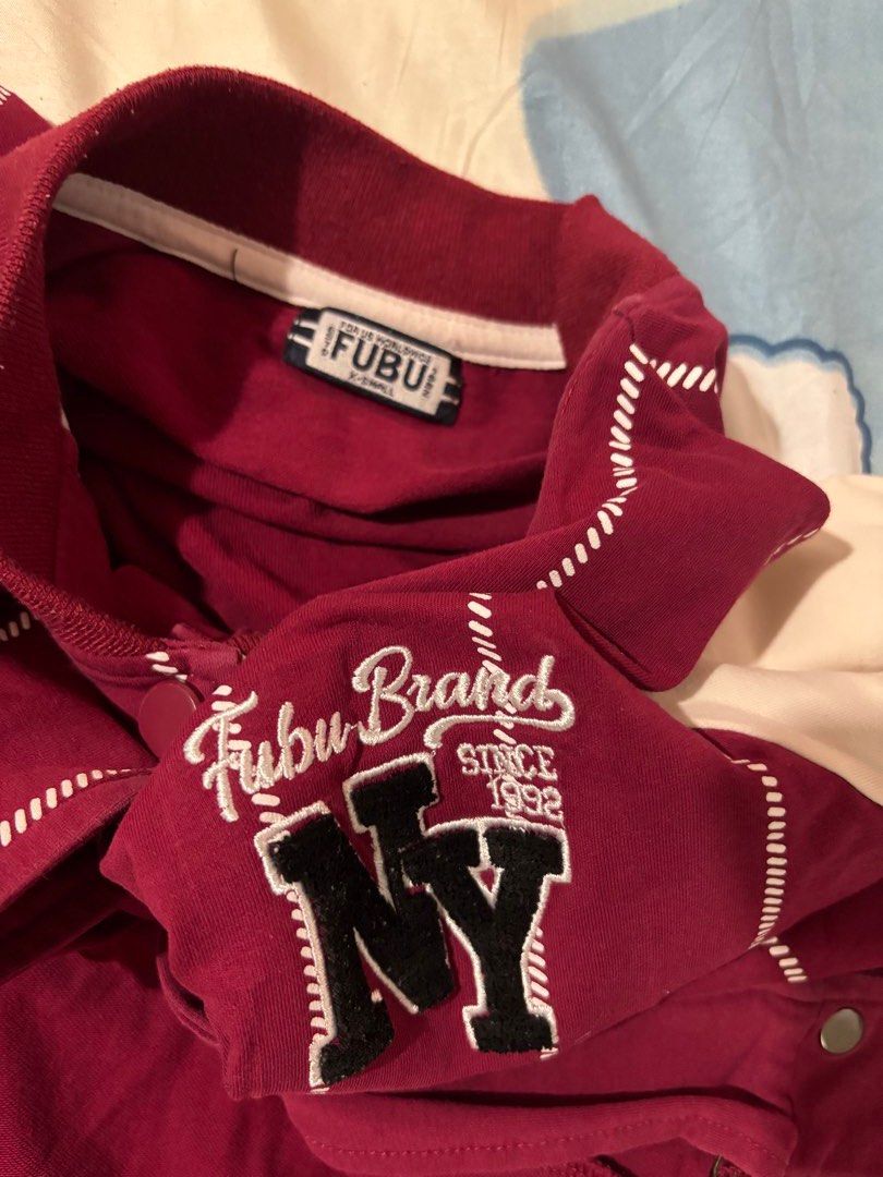 Fubu NY Varsity Jacket (Category: Others Tops) located in Orani. Submitted by cathsclothing (Listing ID 1424597856, Image 2). Description: - Fubu varsity jacket - Color: Maroon and white - Design: Striped body, white sleeves - Features: "NY" logo, Fubu embroidery - Closure: Button-up - Details: Ribbed collar and cuffs - Size: Medium.