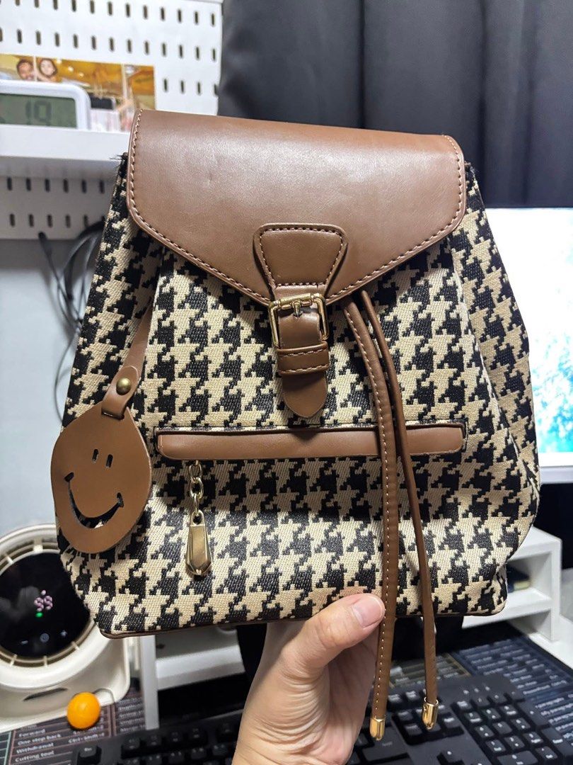 Houndstooth Pattern Backpack (Category: Backpacks) located in Manila. Submitted by dnash29 (Listing ID 1424614626, Image 1). Description: - Houndstooth pattern backpack with brown accents - Flap closure with buckle and drawstring - Adjustable straps - Small front pocket - Includes a cute smiley face charm - Perfect for everyday use.