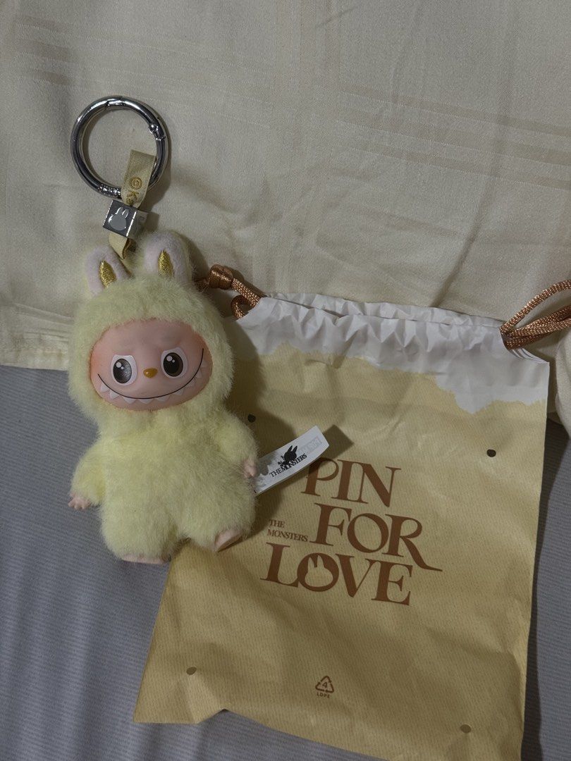 Pop Mart Labubu Pin For Love (Category: Character Goods) located in Valenzuela. Submitted by danabananani (Listing ID 1424627850, Image 1). Description: - Pop Mart Pin For Love Keychain - Features a fluffy yellow character - Smiling face design - Includes a matching drawstring bag - Silver ring keychain - Ribbon with the letter "F" - Character has "F" embroidery on the back - Includes a tag - RFS: Not prio color/letter.
