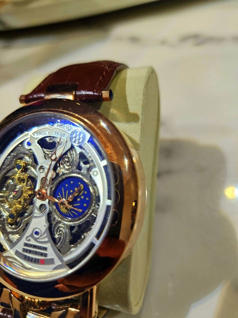 Difful Original Automatic Skeleton Watch (Category: Watches) located in Kuala Lumpur. Submitted by freewhale-6bcf (Listing ID 1424866061, Image 3). Description: Difful Original Automatic watch features a skeleton design, showcasing the intricate inner workings. It has a brown leather strap and a gold-colored case. The watch also has a moon phase indicator. The back of the watch is transparent, revealing the automatic movement. The clasp is brande