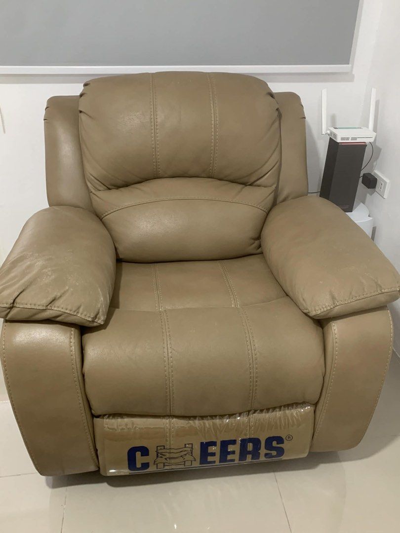 La Sedia Recliner Chair (Category: Chairs) located in Quezon City. Submitted by My_Santos (Listing ID 1424766526, Image 3). Description: Comfortable recliner chair with a beige leather finish. Features a reclining mechanism for added relaxation. The chair has a Cheers logo on the footrest. Includes a white cover for protection. Perfect for living rooms or entertainment areas. RFS: Declutter; comes with free cover Buyer to shoulder lalamove sf aro