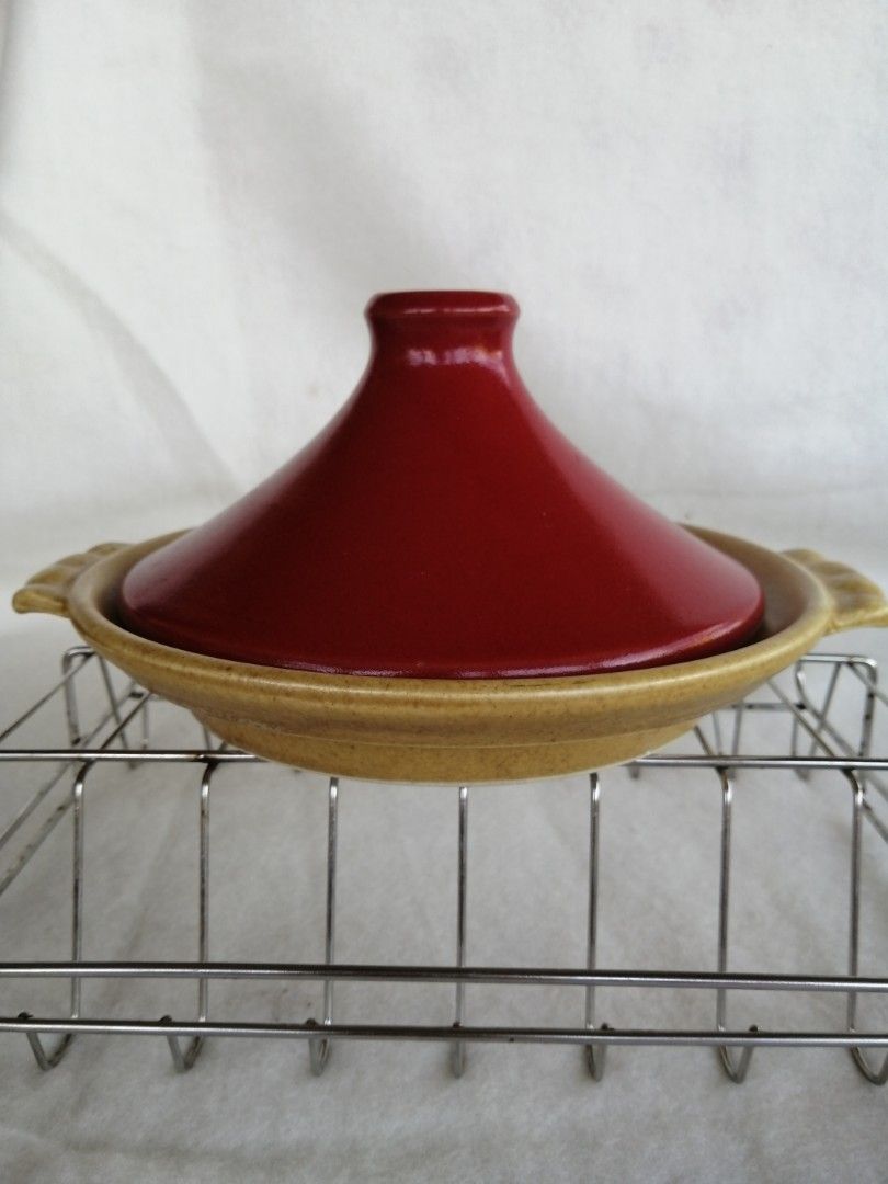 Ceramic Tagine Pot with Lid (Category: Cookware & Accessories) located in Liloan. Submitted by aidolcapz88 (Listing ID 1424939098, Image 1). Description: Ceramic tagine pot features a distinctive conical lid and a round base with handles. The base is a speckled tan color, and the lid is a vibrant red. It is suitable for cooking and serving dishes. The pot is sitting on a metal rack. Size 8"width x 1.5"deep no sign of usage .