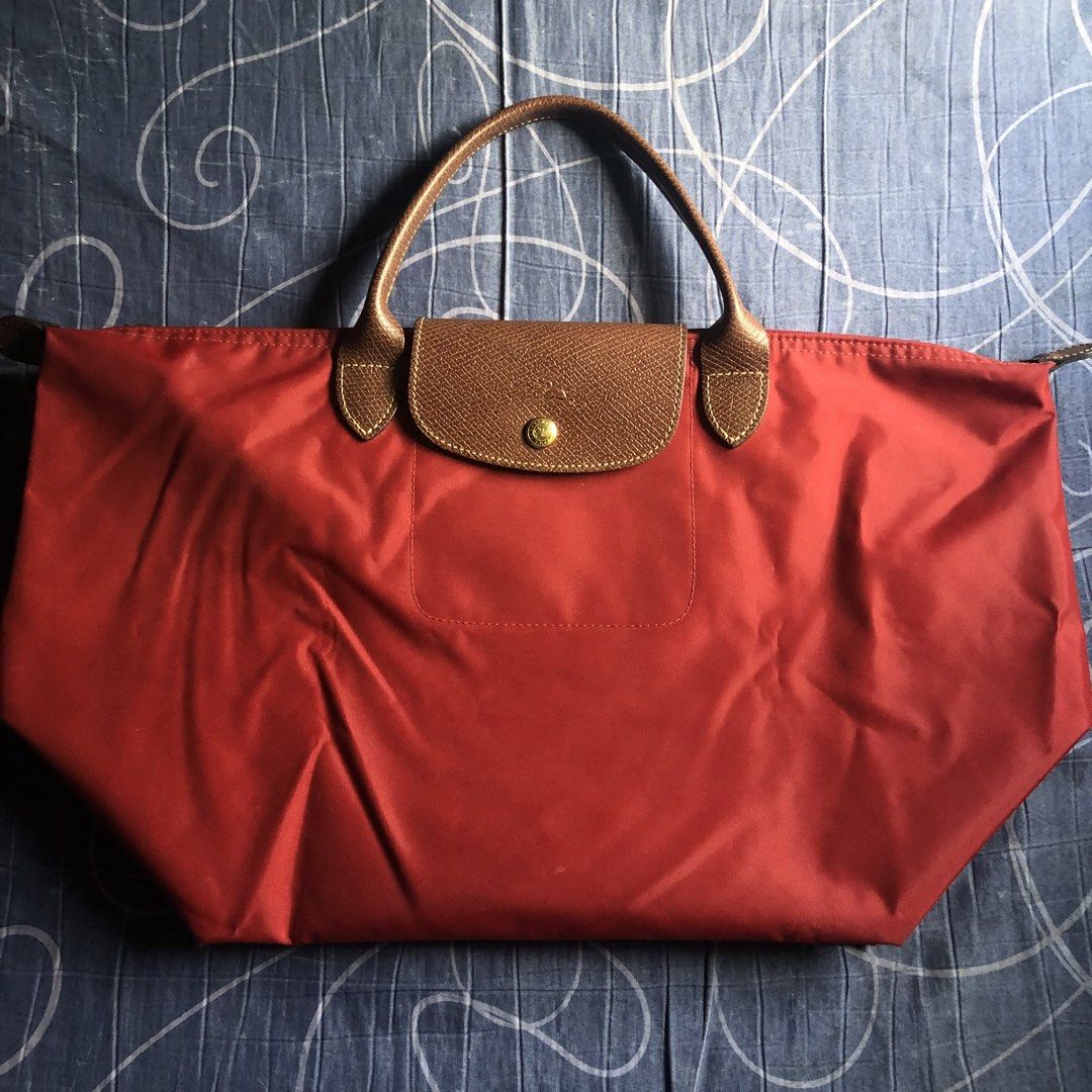 Longchamp Le Pliage M depose Handbag (Category: Luxury Bags & Wallets) located in Mandaluyong City. Submitted by bestofluxielux (Listing ID 1424962566, Image 1). Description: - Authentic Longchamp Le Pliage handbag -Medium size - Red nylon exterior - Brown leather accents - Zipper closure with Longchamp logo charm - Beige lining - Interior pocket - Snap closure - Longchamp logo on front -With staining inside - Made in China.
