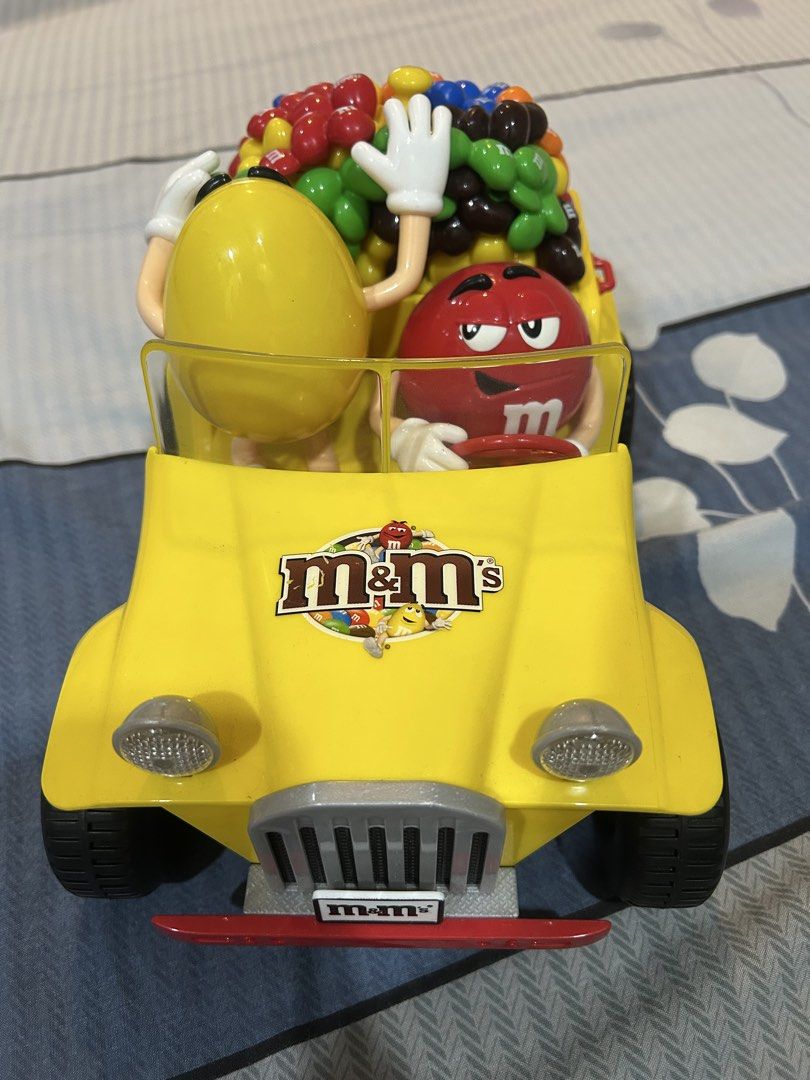 M&M's Candy Dispenser Car (Category: Vehicle & Diecast Models) located in Manila. Submitted by alainachu (Listing ID 1425037071, Image 2). Description: Fun M&M's candy dispenser shaped like a yellow car. It features the M&M's characters, with the red M&M driving and the yellow M&M waving. The car is filled with colorful M&M's candies. It has a clear windshield and headlights. The back of the car has a green compartment. Loc: San Juan City.