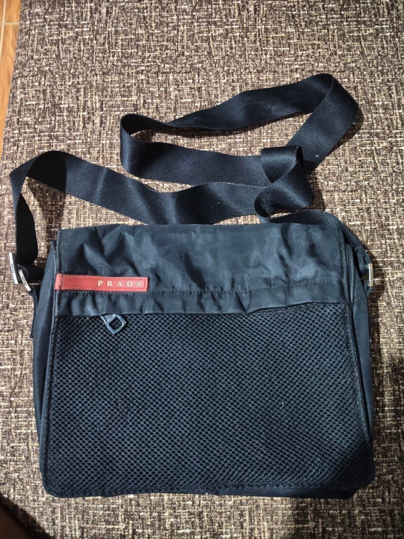 Prada Black Messenger Bag (Category: Luxury Bags & Wallets) located in Caloocan City. Submitted by balizaclar77072 (Listing ID 1425031232, Image 1). Description: Black Prada messenger bag with a mesh front pocket and a red Prada logo. Features a black adjustable strap. The bag has a zipper closure. The bag is rectangular in shape..
