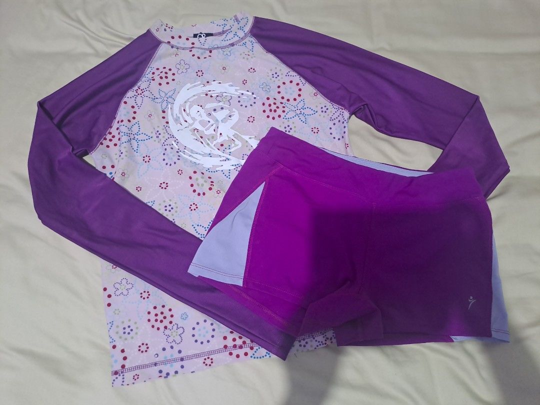 Purple Floral Swimsuit Set (Category: Bikinis & Swimsuits) located in Ajuy. Submitted by ainakou (Listing ID 1424927156, Image 1). Description: Swimsuit set features a long-sleeved top with a floral pattern and purple sleeves. It includes matching purple shorts with light purple side panels. The top has a white design on the front. Perfect for swimming or water activities..