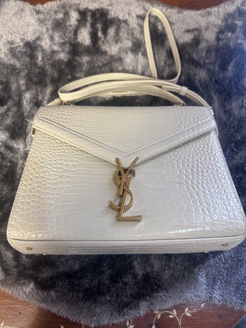 YSL White Crocodile-Embossed Handbag (Category: Luxury Bags & Wallets) located in Manila. Submitted by mavsthriftstore (Listing ID 1424929847, Image 2). Description: Elegant YSL handbag in white with a crocodile-embossed finish. Features a top handle and a detachable shoulder strap. The bag has a gold-tone YSL logo on the front. It has a structured shape with a flap closure..