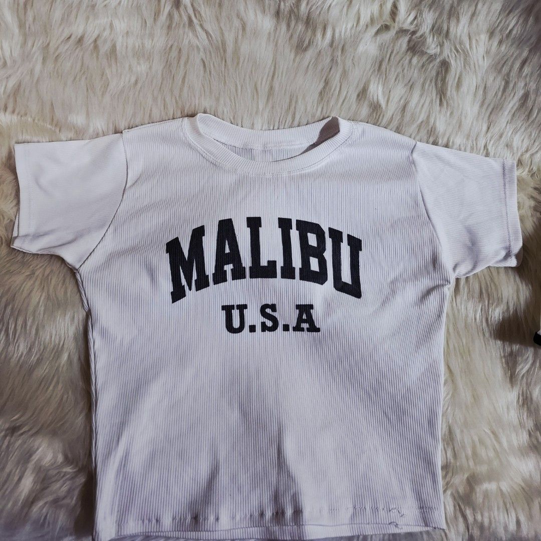 Malibu U.S.A. White Ribbed Crop Top (Category: Shirts) located in Lipa City. Submitted by kimathy.declutters (Listing ID 1425069972, Image 2). Description: White ribbed crop top featuring "MALIBU U.S.A." printed in black. The shirt has short sleeves and a round neckline. The shirt is white with black lettering..