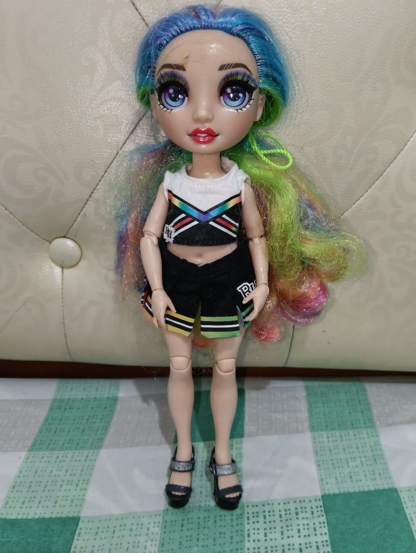 Rainbow High Cheer Doll (Category: Kids Toys) located in Angono. Submitted by lala_tan (Listing ID 1425243405, Image 1). Description: Rainbow High Cheer doll with vibrant rainbow hair and detailed makeup. She is wearing a white and black crop top, black shorts with rainbow stripes, and black sandals. The doll has articulated limbs and is ready for play or display. have flaws sa fez.