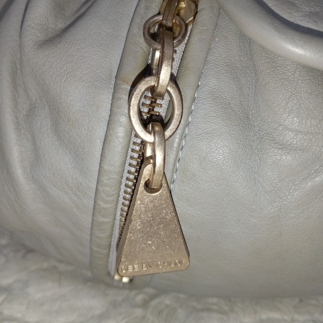 See by Chloe Grey Leather Handbag (Category: Luxury Bags & Wallets) located in Baguio. Submitted by sheren_signatures (Listing ID 1425170475, Image 3). Description: See by Chloe handbag features a soft grey leather exterior with gold-toned hardware. It has a flap closure and two zippered pockets on the front. The interior is lined with a pink fabric and includes a small pocket. The bag has a shoulder strap and a tassel detail. Made in Morocco..