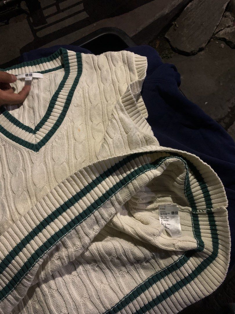 Uniqlo Cable Knit Vest (Category: Vests) located in Manila. Submitted by euphoriathriftco (Listing ID 1425223562, Image 2). Description: Cream-colored cable knit vest from Uniqlo. Features a V-neck design with green trim along the neckline and hem. The vest has a sleeveless design. The tag is visible in the image. Made of a knit material..