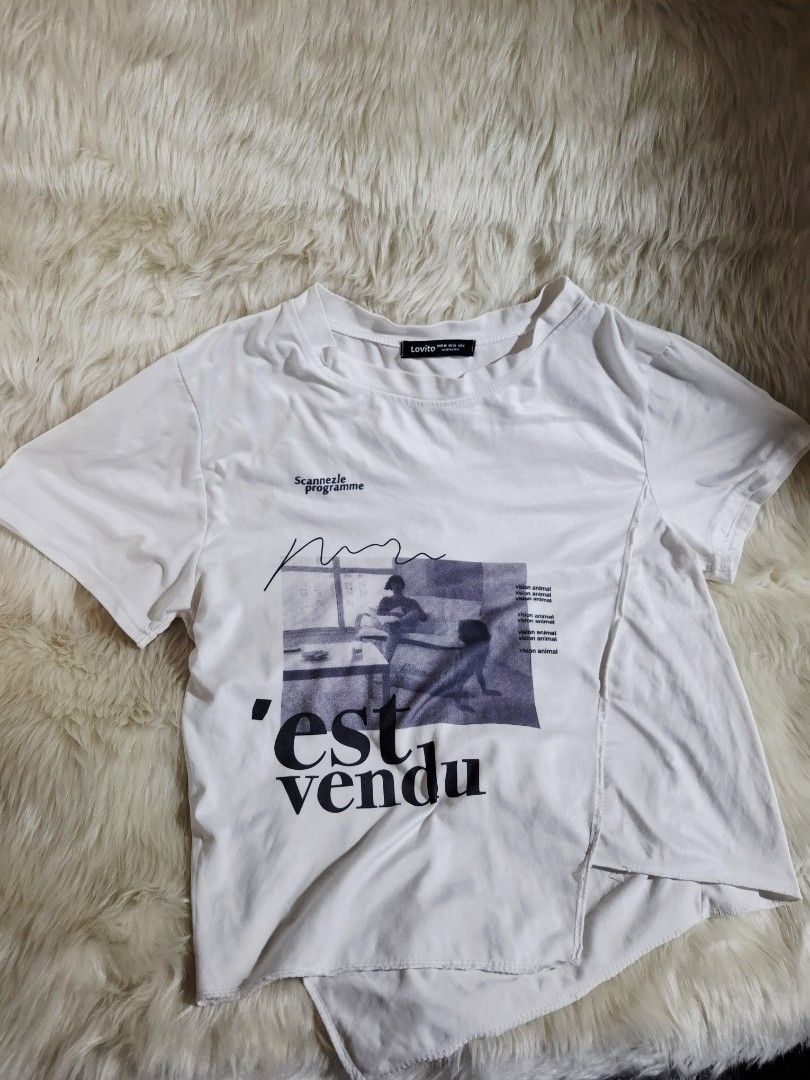 LOVITO White Graphic Tee (Category: Shirts) located in Lipa City. Submitted by kimathy.declutters (Listing ID 1425069980, Image 2). Description: White t-shirt with a unique graphic print. Features a crew neck and short sleeves. The graphic includes the words "'est vendu" and a black and white image. The shirt has an asymmetrical design on the front. The brand label is visible on the neck..