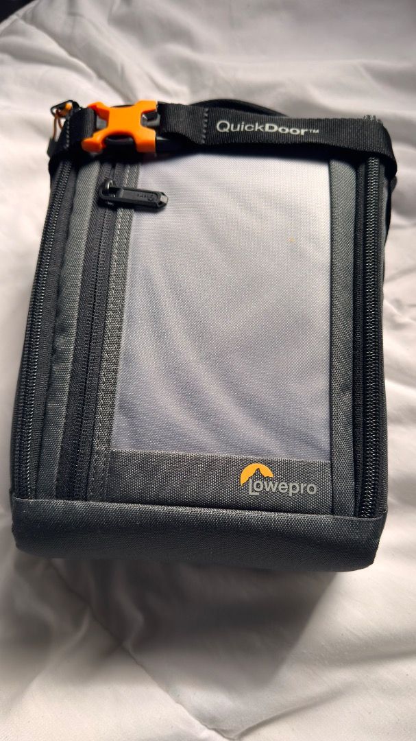 Lowepro QuickDoor 2.5 Camera Bag (Category: Camera Bags & Carriers) located in Antipolo. Submitted by littlefoot15p (Listing ID 1425315868, Image 1). Description: Lowepro camera bag features a QuickDoor design for easy access. It has a gray exterior with a black strap and orange accents. The interior is bright orange with adjustable compartments. It includes a front pocket and a top handle. The bag is designed to protect camera equipment..