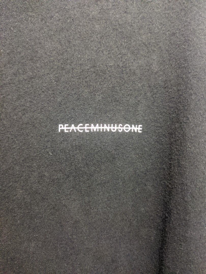 PEACEMINUSONE Black Oversized T-shirt (Category: Tshirts & Polo Shirts ) located in Dasmarinas. Submitted by _thrift.lang_ (Listing ID 1425370190, Image 2). Description: Black oversized t-shirt from PEACEMINUSONE. Features a small white logo on the front and the brand's logo on the neck label. The back of the neck label has a printed quote. The shirt has a unique design with a tie detail at the bottom..