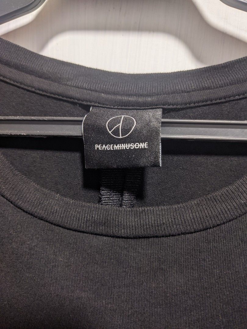 PEACEMINUSONE Black Oversized T-shirt (Category: Tshirts & Polo Shirts ) located in Dasmarinas. Submitted by _thrift.lang_ (Listing ID 1425370190, Image 3). Description: Black oversized t-shirt from PEACEMINUSONE. Features a small white logo on the front and the brand's logo on the neck label. The back of the neck label has a printed quote. The shirt has a unique design with a tie detail at the bottom..